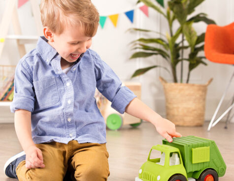 A kid playing with a green toy recycling truck in a playroom.